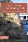 A large stack of hay bales serving as a livestock windbreak with a barn in the background.