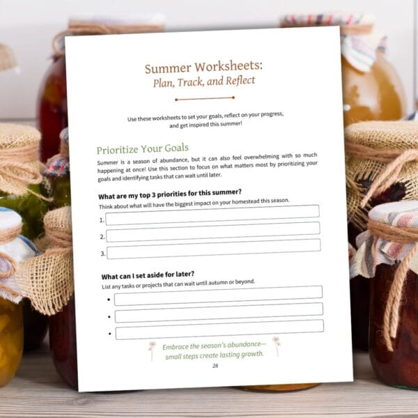 A printed page from the workbook showing "Summer Worksheets: Plan, Track, and Reflect," with prompts to prioritize homestead goals. The page is propped against a backdrop of jars filled with preserved foods wrapped in rustic fabric and twine.