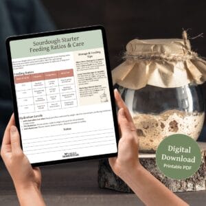 A person holding a tablet displaying the "Sourdough Starter Feeding Ratios & Care" page with a jar of sourdough starter covered with parchment and twine in the background.