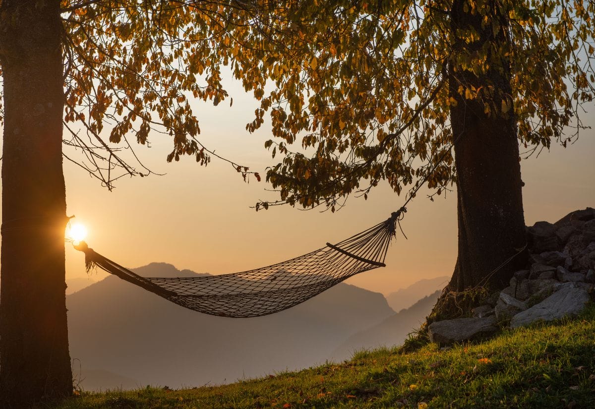 A hammock hanging between two trees at sunset with a serene mountain view in the background.