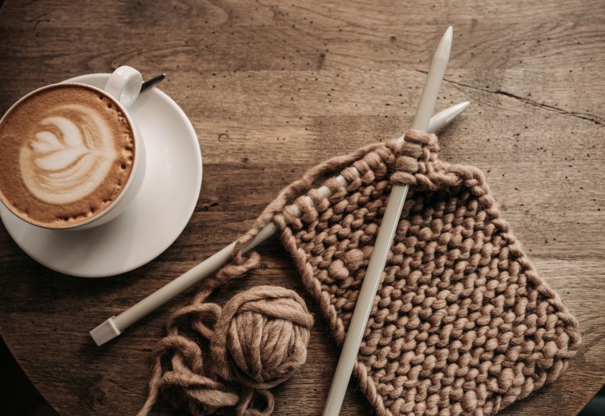 A cozy scene with a cup of coffee and a knitting project on a wooden table.