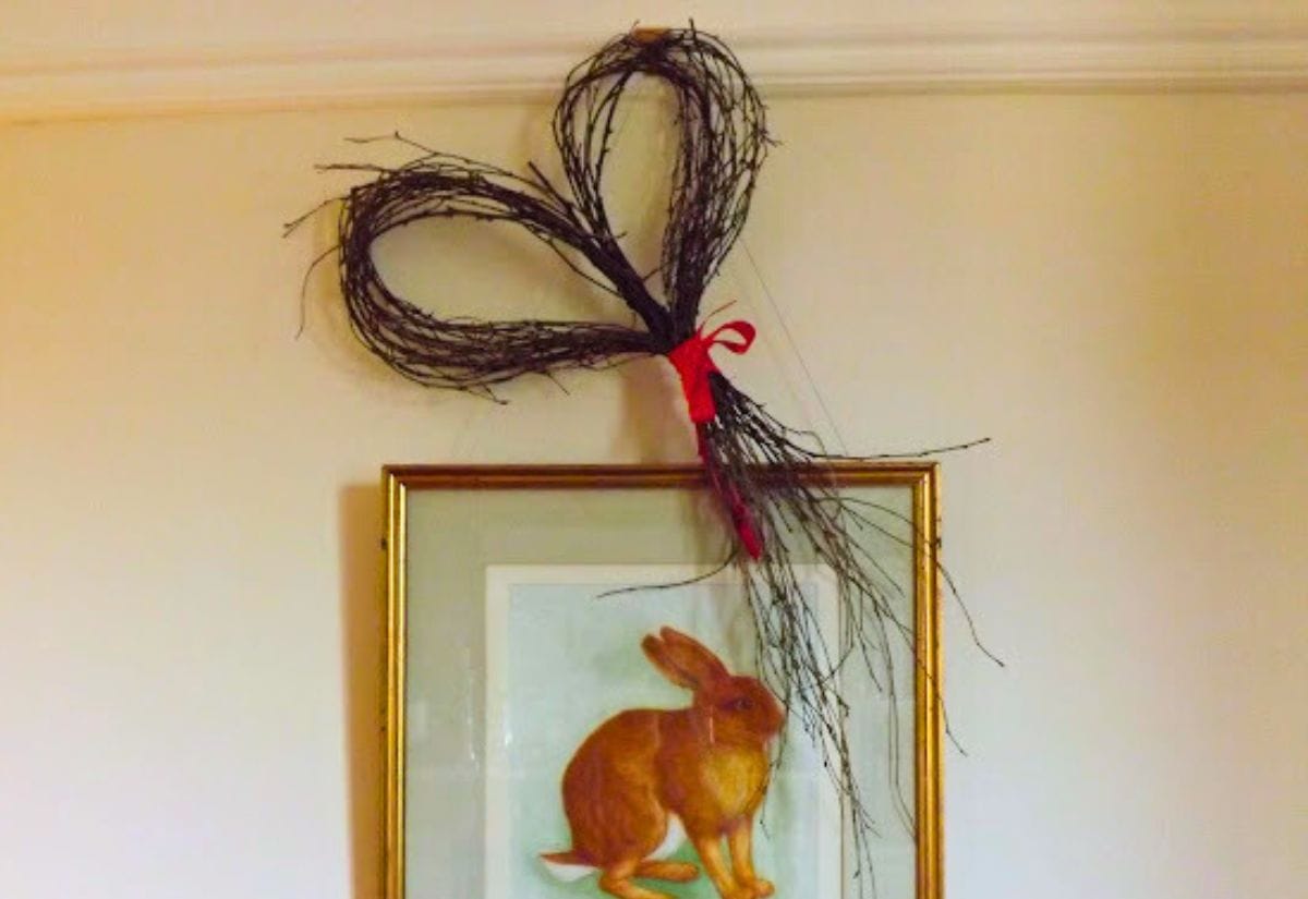 A heart-shaped wreath crafted from twigs and tied with a red ribbon, displayed on a wall.