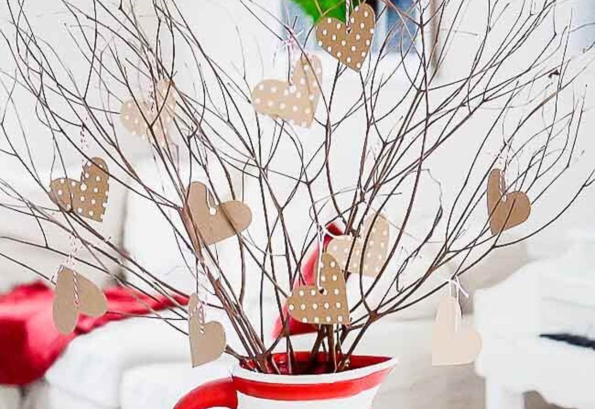 A Valentine tree made of twigs arranged in a red and white striped vase, decorated with heart-shaped paper ornaments.