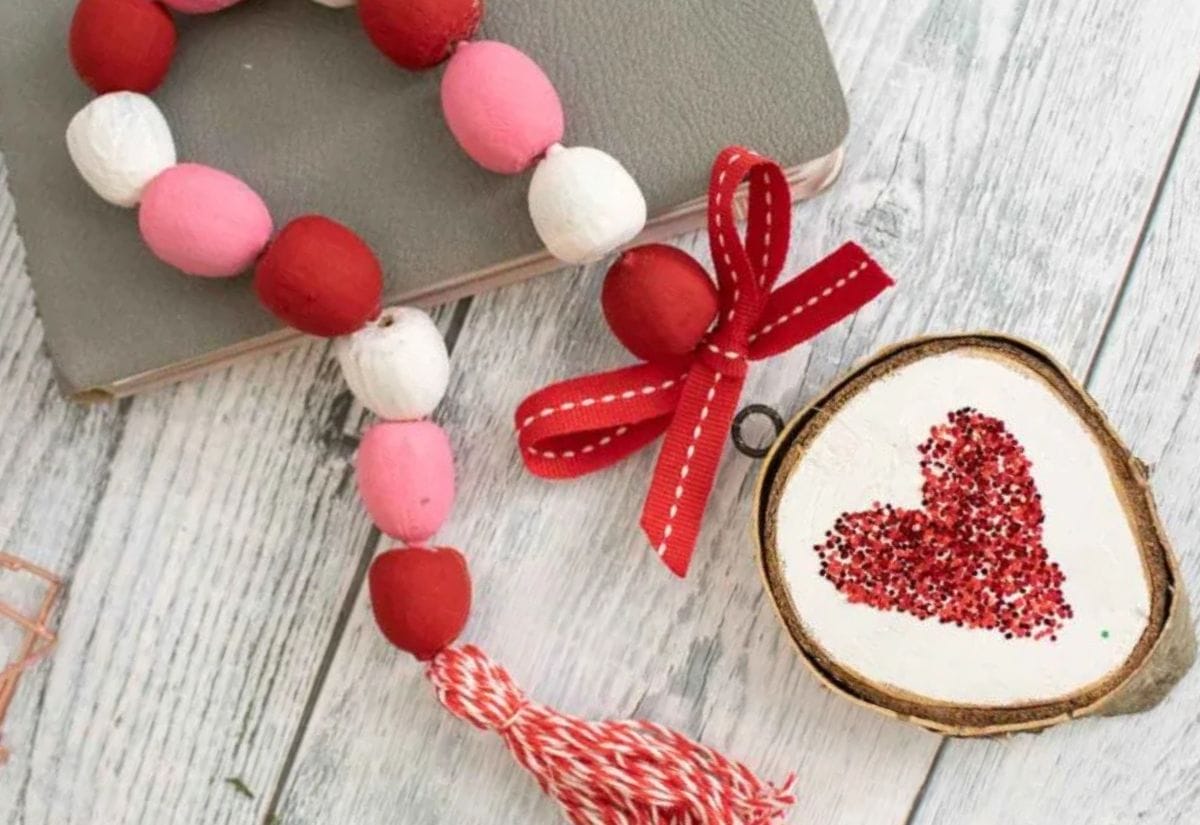 Close-up of a handmade garland with painted acorns in pink, red, and white, paired with a wooden ornament featuring a glitter heart.