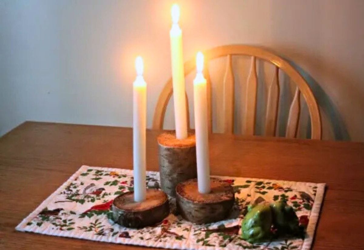 A rustic centerpiece featuring three birch wood candle holders with glowing taper candles.