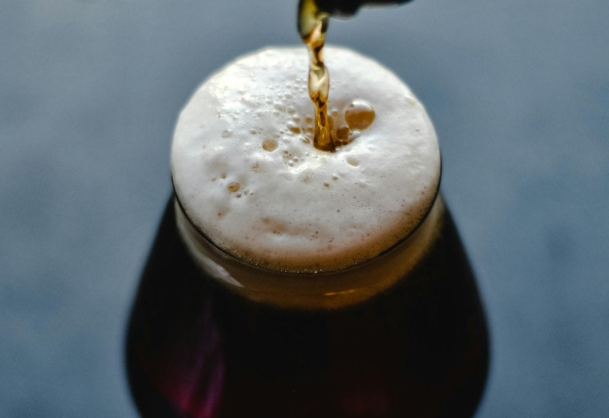 A freshly poured Irish stout being served, with frothy foam cascading down the side of the glass.