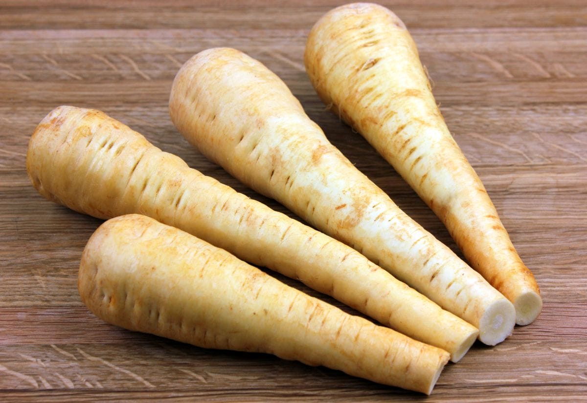 Four fresh parsnips laid out on a wooden cutting board, showing their golden skin and tapered shape.