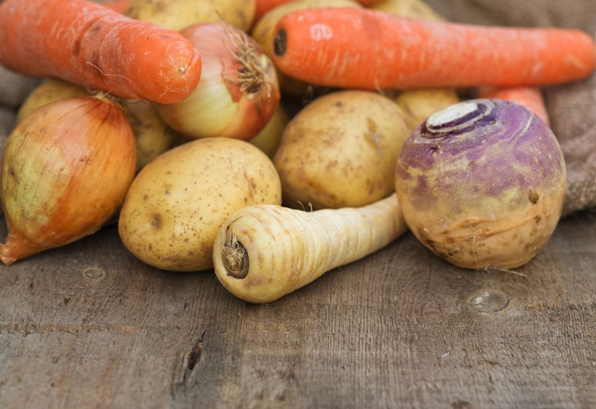 A mix of potatoes, onions, carrots, parsnips, and a turnip on a rustic wooden surface, ready for soup preparation.