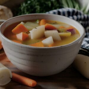 A steaming bowl of Irish farmhouse soup with diced potatoes, carrots, parsnips, and turnips in a rich broth.