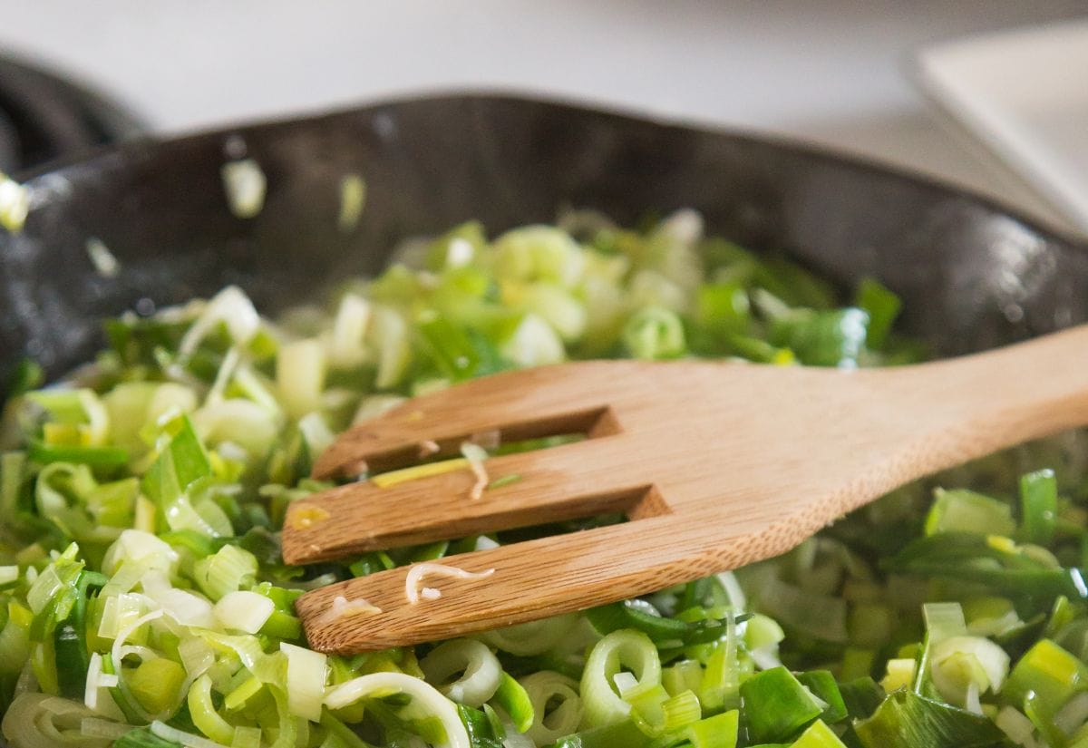 Freshly chopped leeks sautéing in a cast iron skillet, stirred with a wooden spatula.