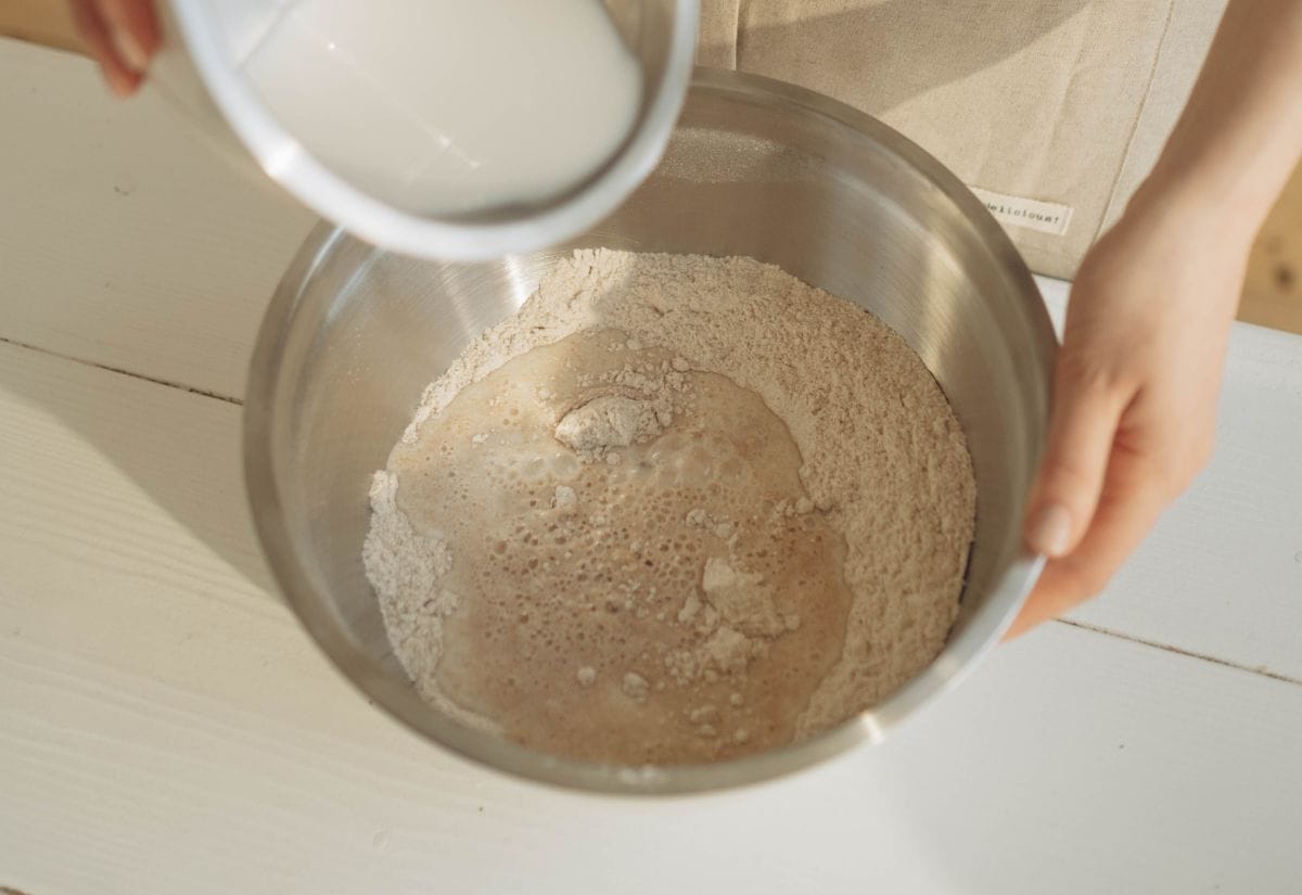 Pouring buttermilk into the bowl of dry ingredients to prepare the dough for Irish soda bread.