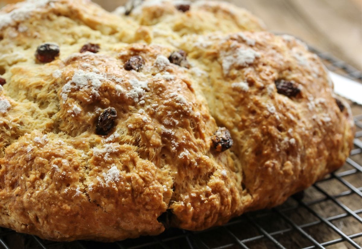 A close-up of a golden-brown Irish soda bread resting on a cooling rack, dusted with flour.