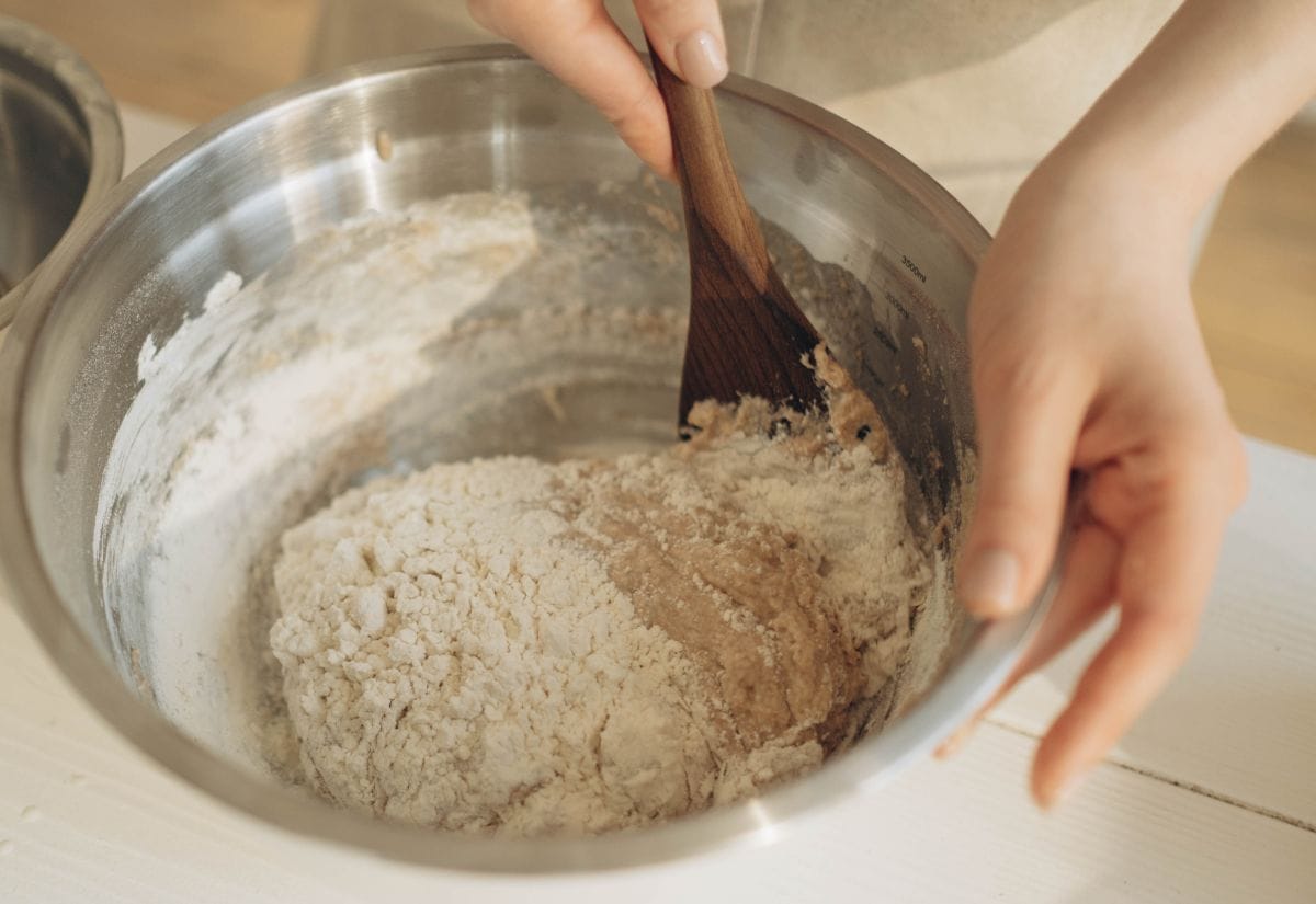 A person stirring together dry and wet ingredients in a metal mixing bowl to form Irish soda bread dough.