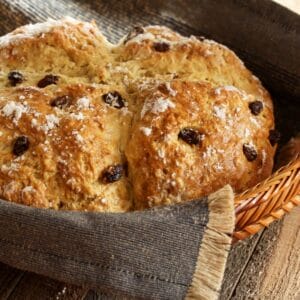 A beautifully golden Irish soda bread in a woven basket, wrapped in a linen cloth for serving.