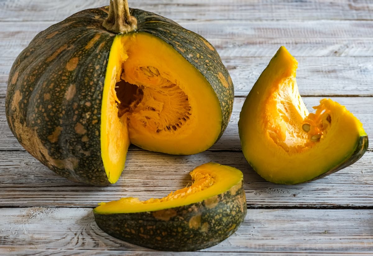 A hybrid squash cut into sections, revealing seeds inside, placed on a rustic wooden table.