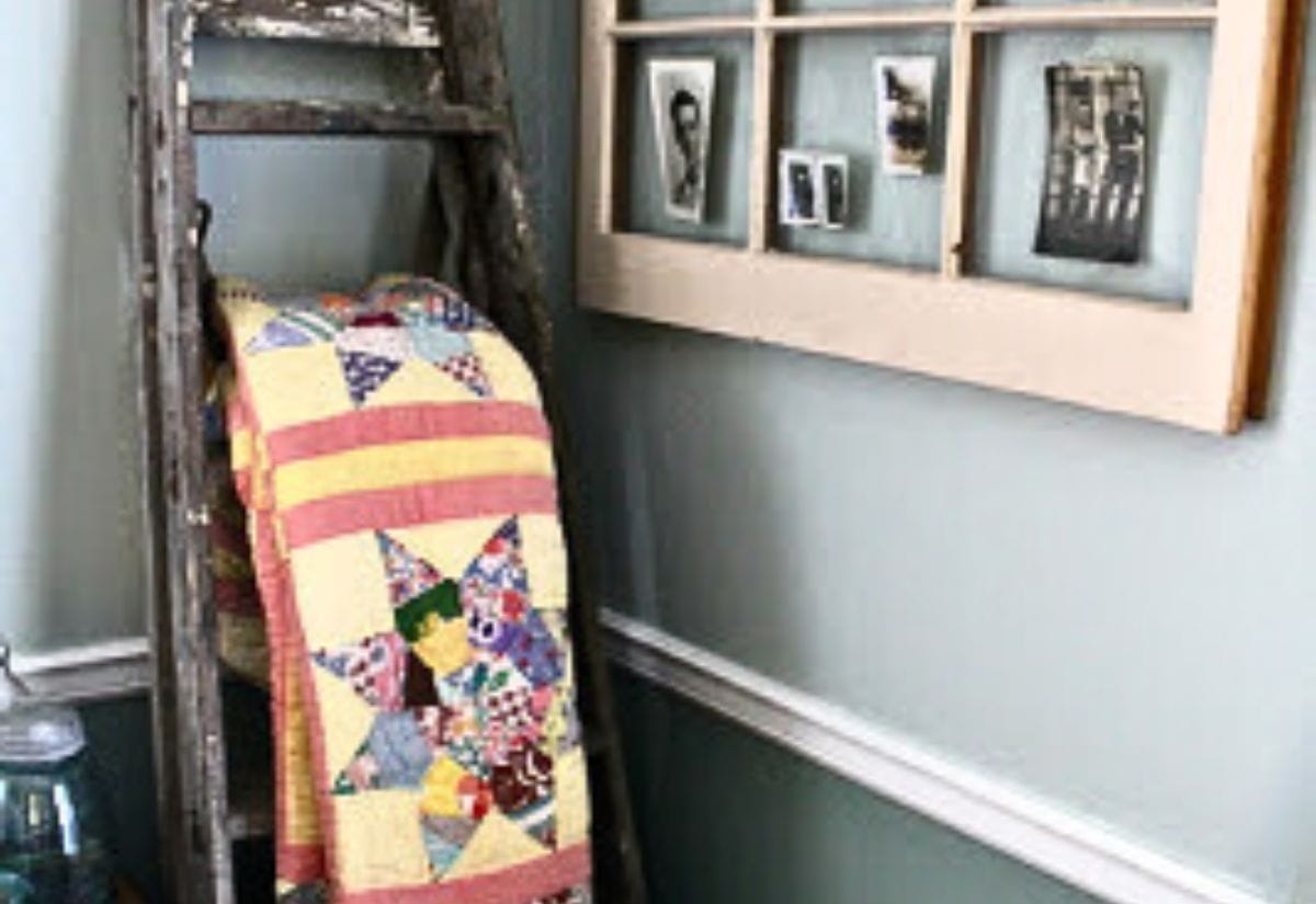 An old wooden ladder repurposed as a cozy quilt rack, paired with a vintage window frame turned into a rustic photo display.