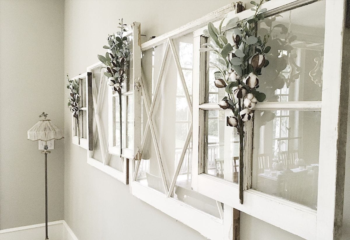 A set of repurposed vintage windows, mounted on a wall and adorned with cotton stems and eucalyptus, creating a stunning farmhouse-inspired display.