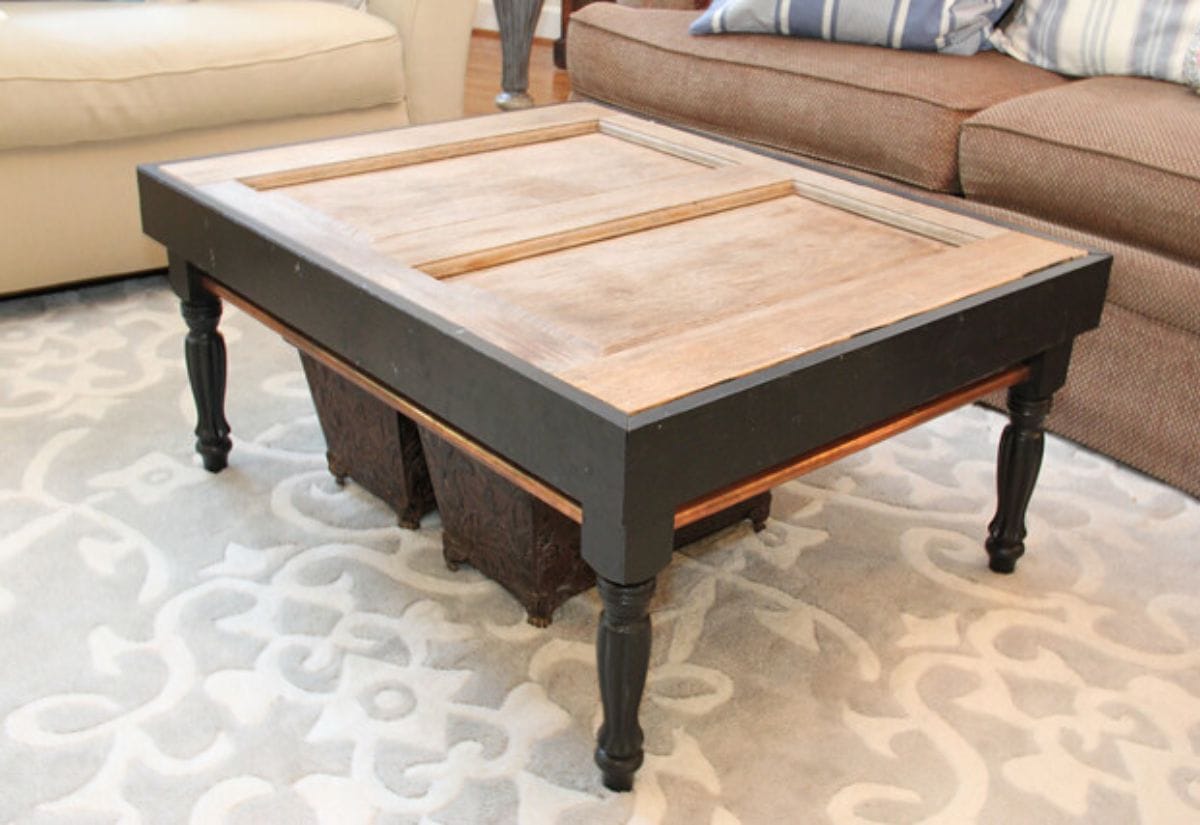 A rustic farmhouse coffee table made from a repurposed wooden door, with sturdy black legs and a distressed finish, adding character to the living room.