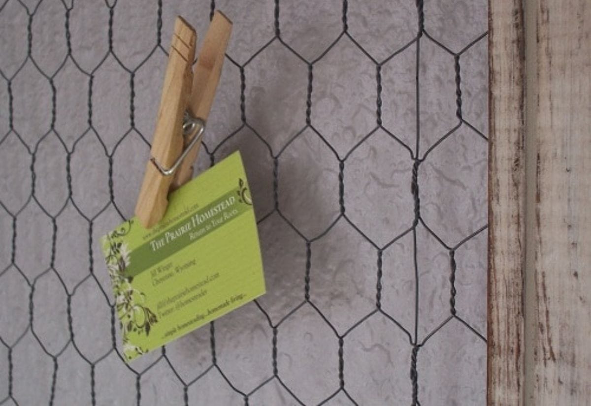 A rustic DIY organizer made from an old picture frame with chicken wire, featuring a clothespin holding a business card, perfect for farmhouse-style organization.