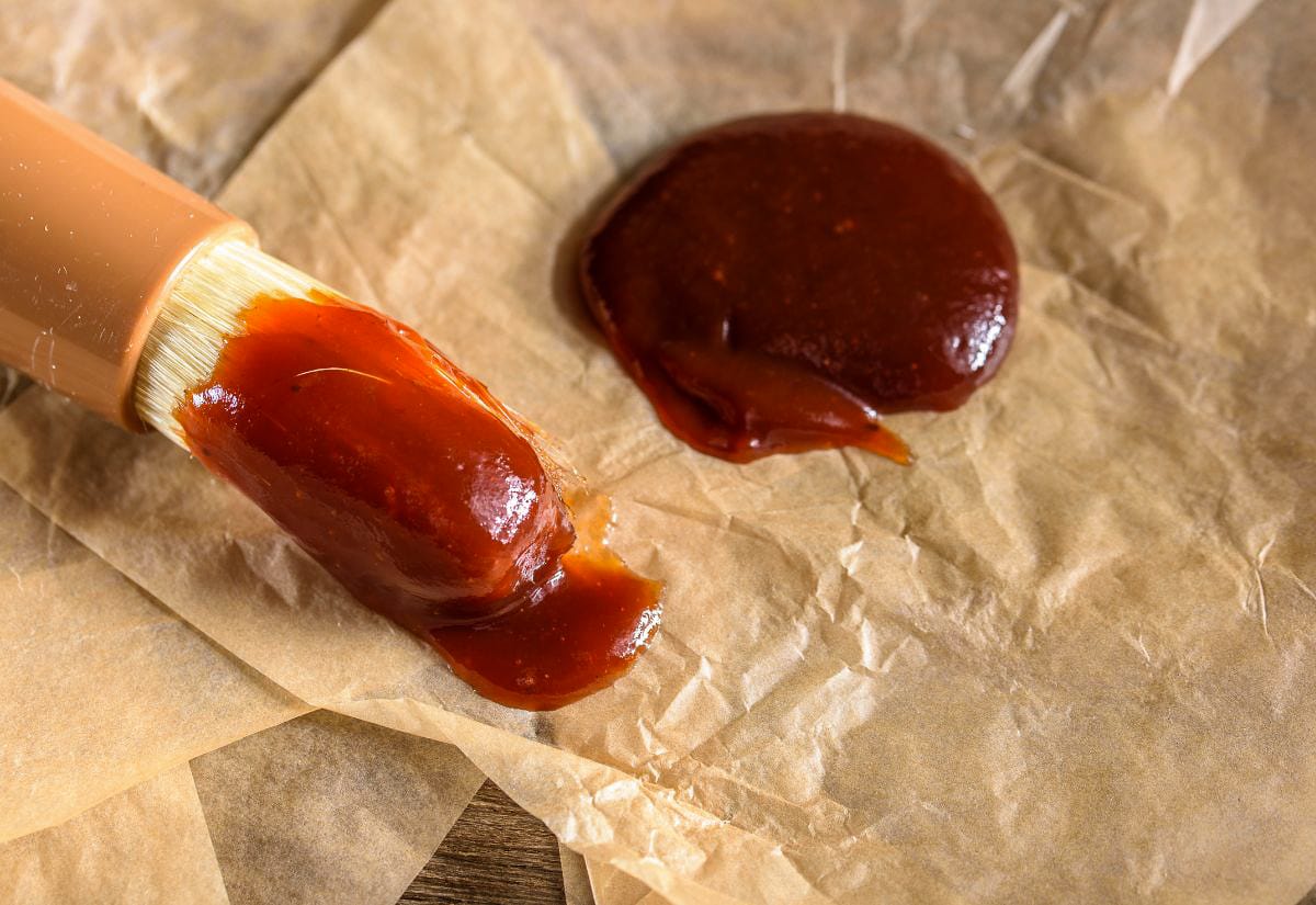 BBQ sauce brushed on parchment paper with a basting brush, showing its thick and smooth texture.