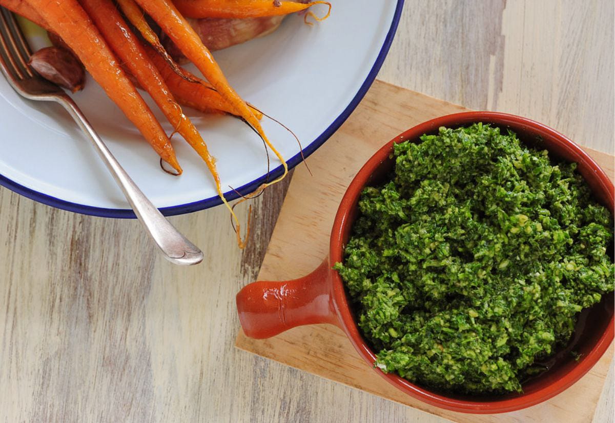 A bowl of vibrant green carrot top pesto next to a plate of roasted carrots.