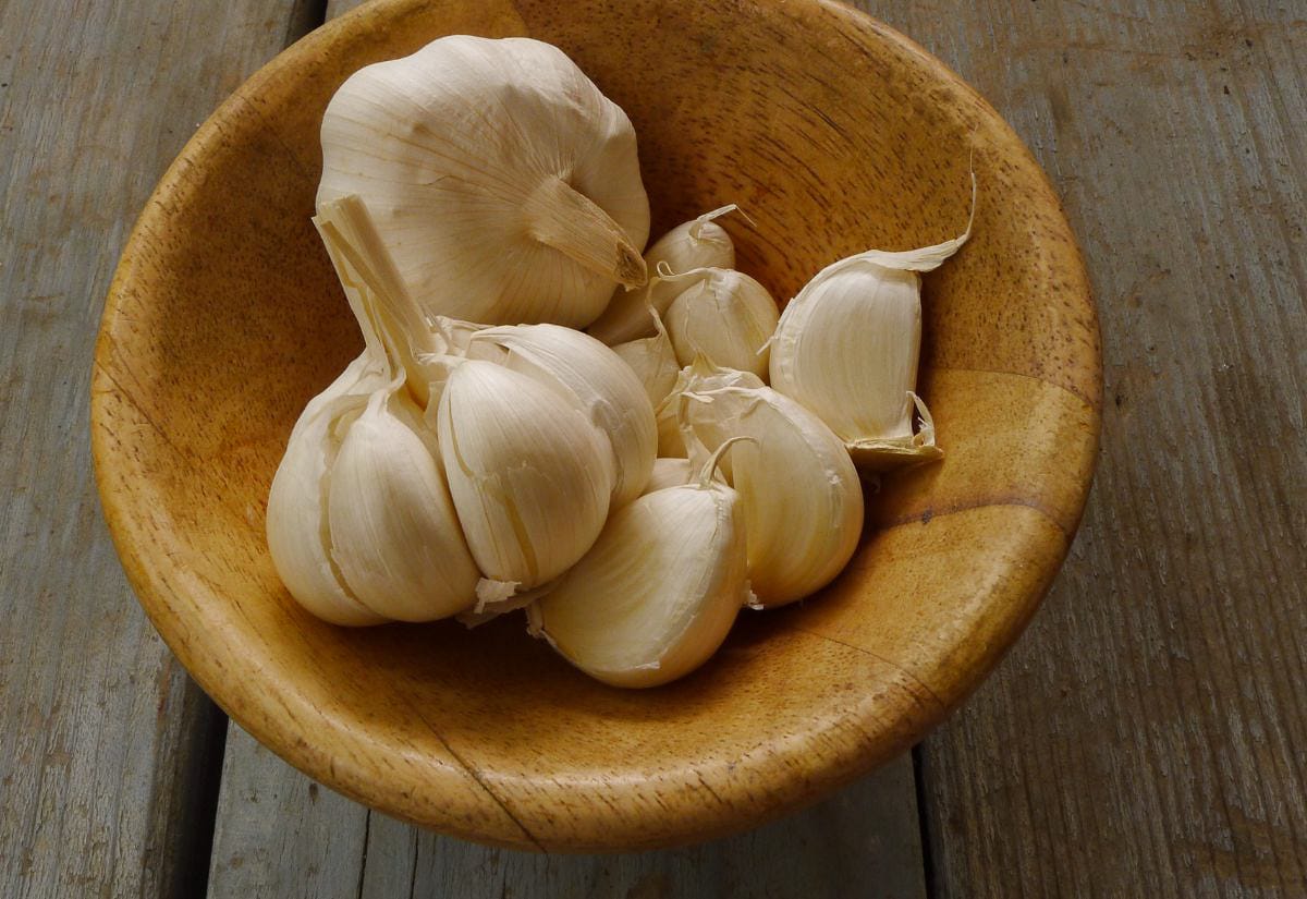 A wooden bowl filled with whole garlic bulbs and separated cloves sitting on a rustic wooden surface.