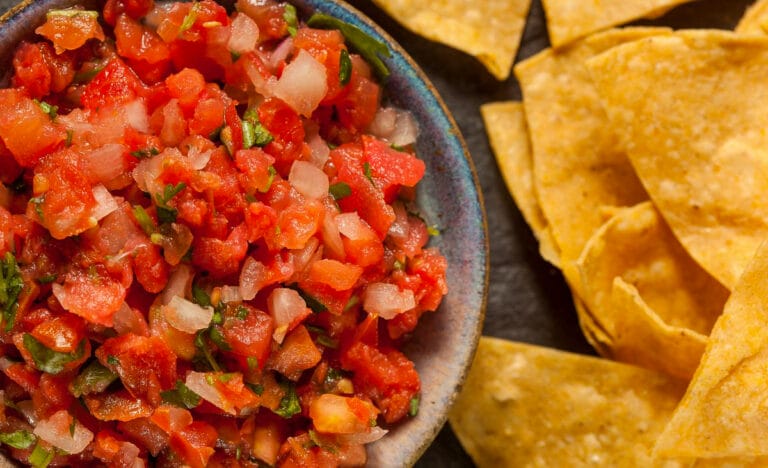 Overhead close-up of fresh tomato salsa in a ceramic bowl, filled with chopped tomatoes, onions, and herbs, served next to crispy tortilla chips.