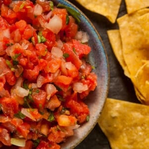 Close-up of a bowl of fresh salsa made with diced tomatoes, onions, and cilantro, served alongside crispy tortilla chips.
