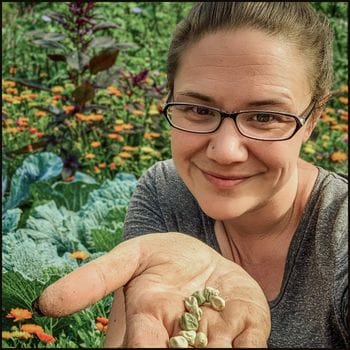 Jessica Knowles holding pea seeds in her hand, smiling in front of a colorful vegetable and flower garden with cabbage, calendula, and amaranth.
