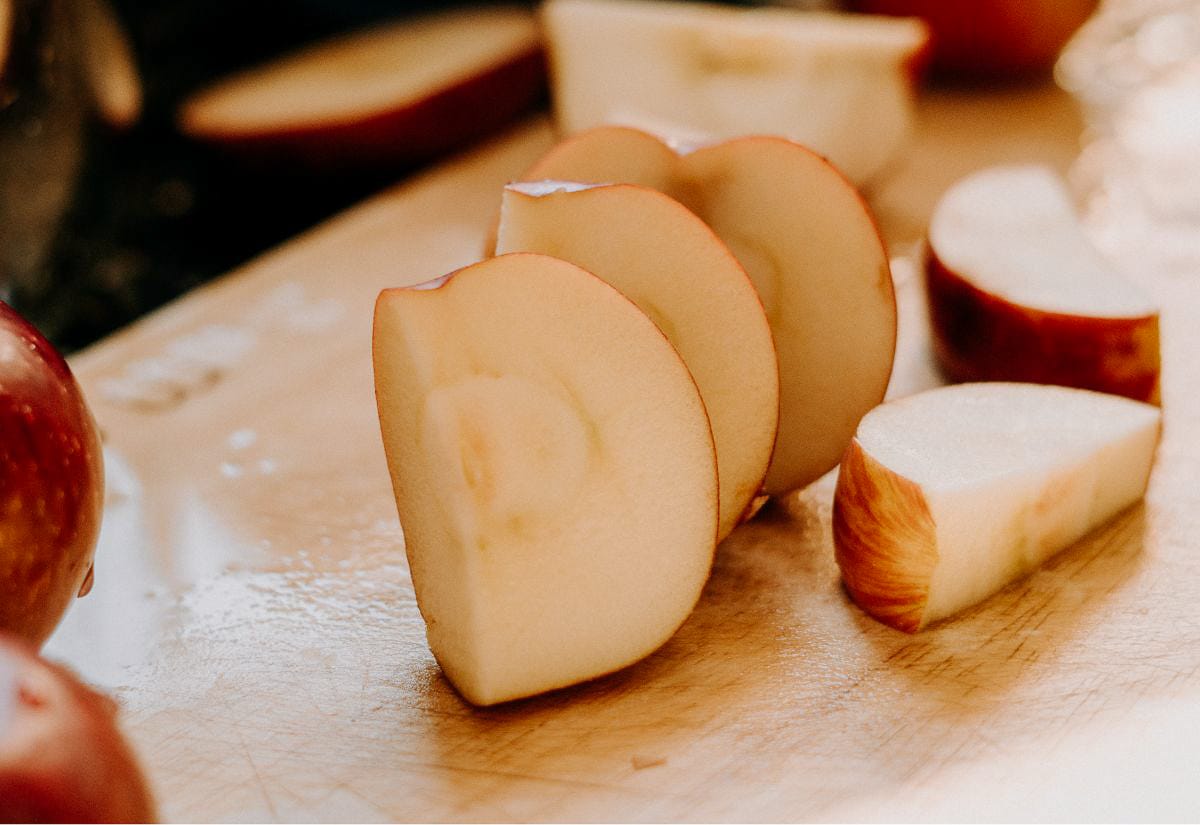 Fresh apples sliced into wedges on a wooden cutting board, starting to show the early stages of browning.