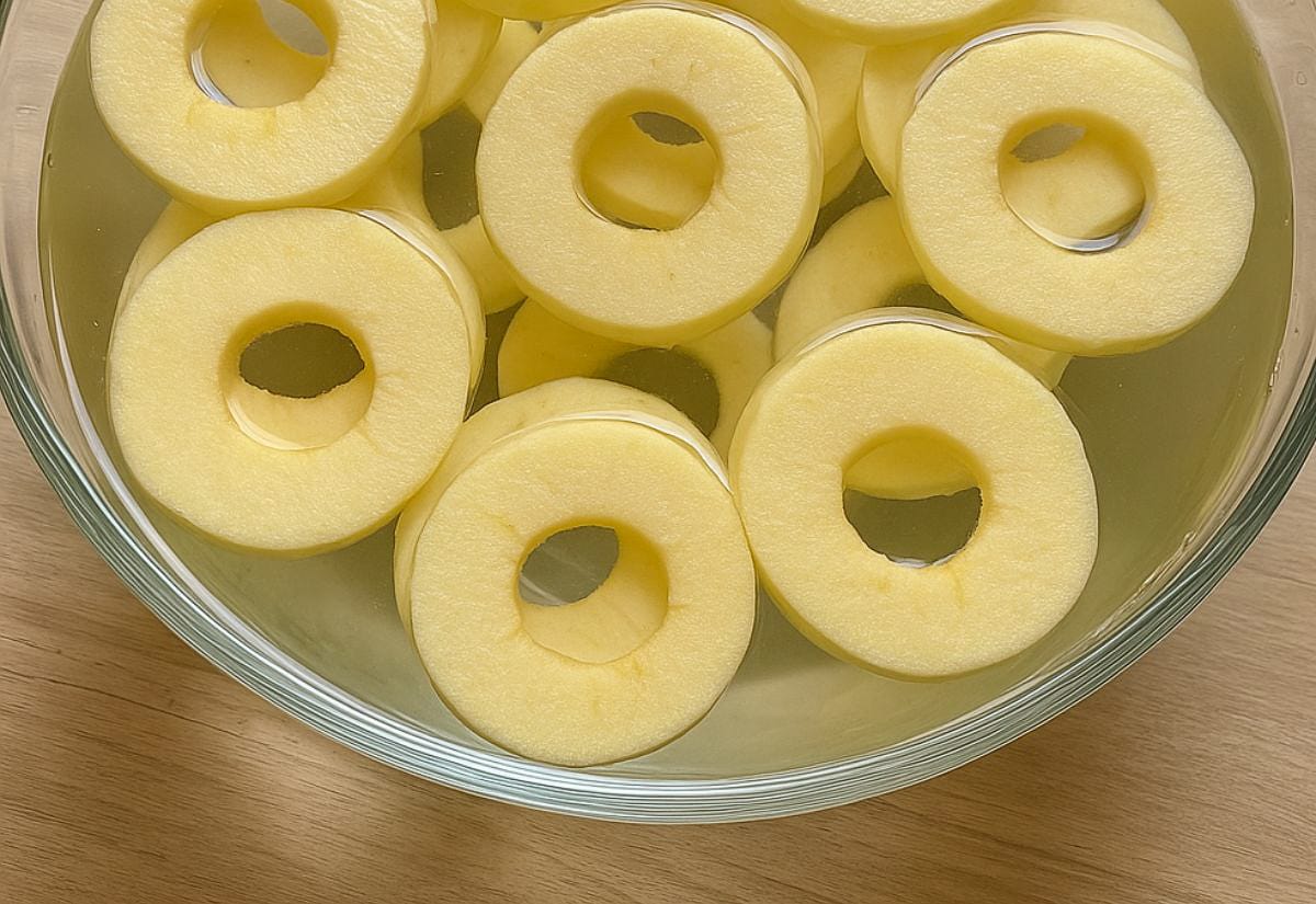 Freshly cored apple rings soaking in a lemon water solution to prevent browning before dehydrating.