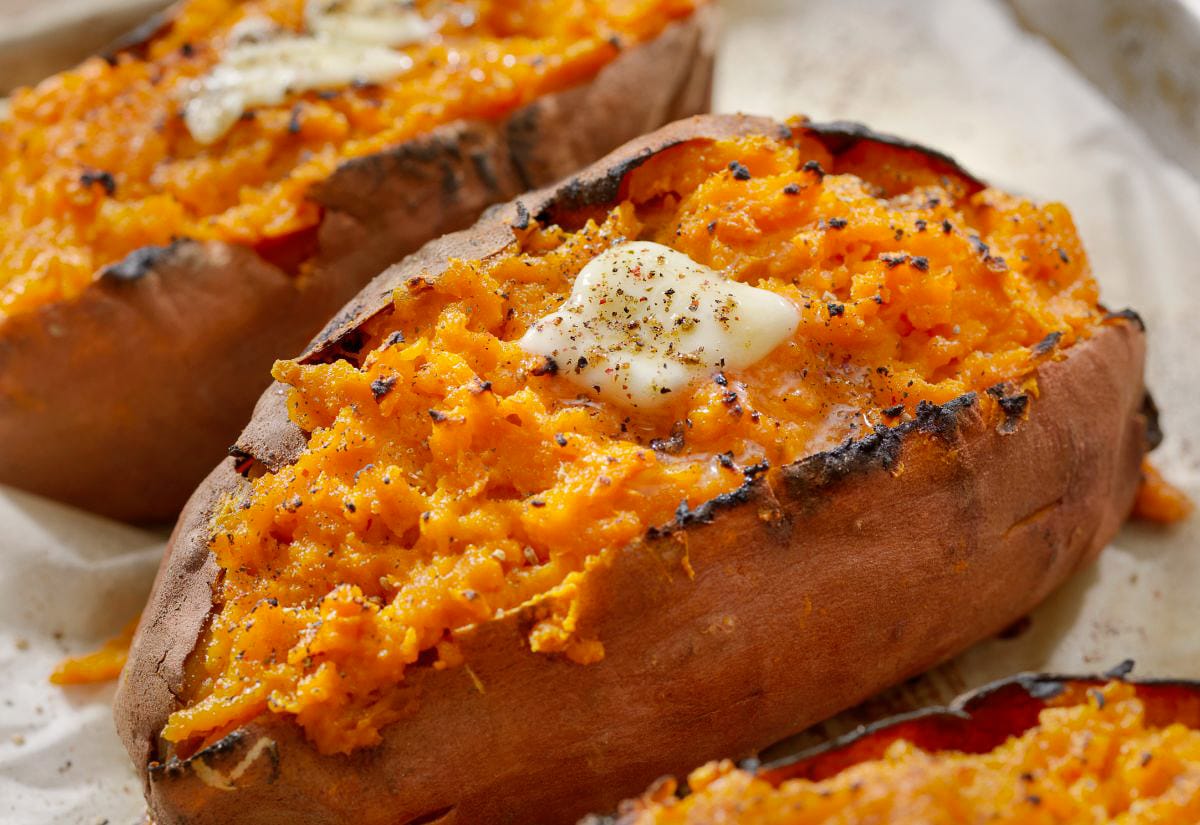 Baked sweet potatoes split open with melted butter and cracked pepper on top, illustrating how properly cured potatoes cook up tender and flavorful.