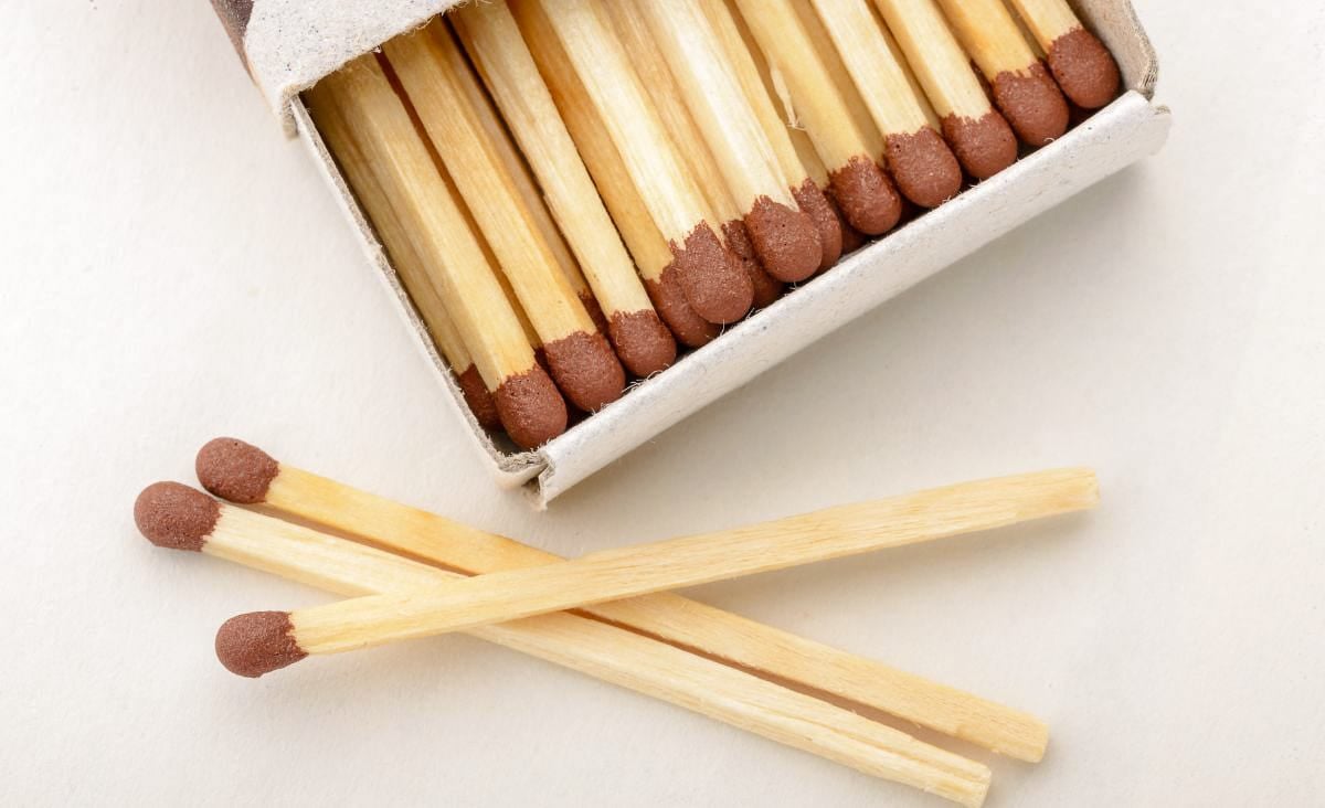 Close-up photo of an open box of wooden matches, some resting on a white surface, ready for lighting a wood stove or fire.