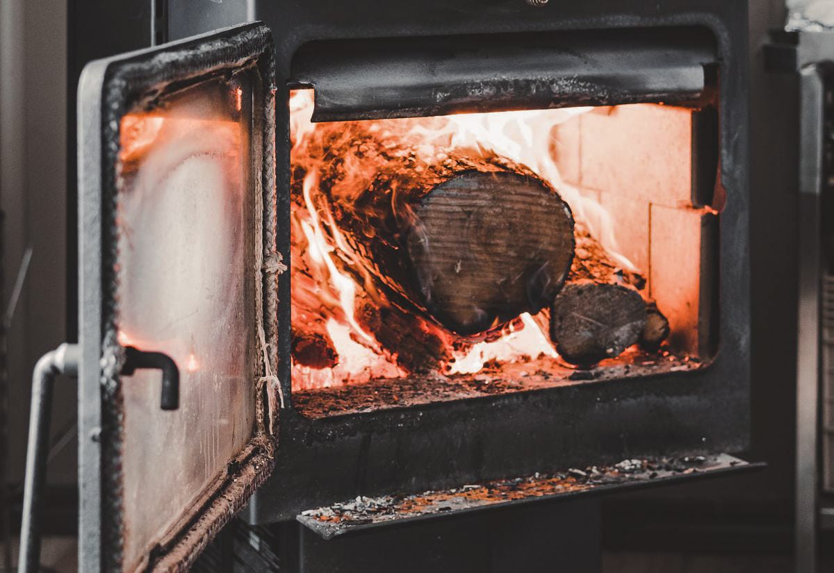 Wood stove with the door open and a bright, roaring fire inside, burning large logs without kindling.