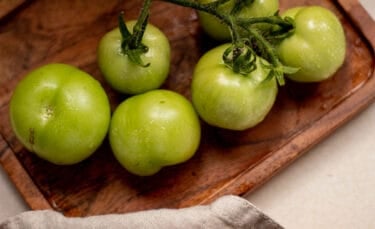 Close-up of several firm green tomatoes on a wooden tray, showing their smooth skin and garden-fresh color before ripening.