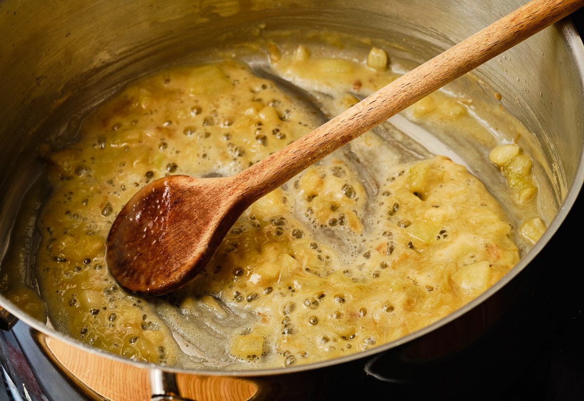 Golden roux bubbling in a stainless-steel saucepan as a wooden spoon stirs the fat and flour together.