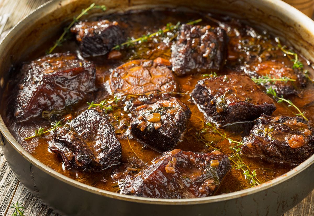 Pan of slow-braised beef short ribs simmering in a rich, brown pan-dripping sauce with thyme sprigs.