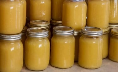 Rows of pint and quart jars filled with homemade canned applesauce, sealed with metal lids and stacked closely together on a counter.