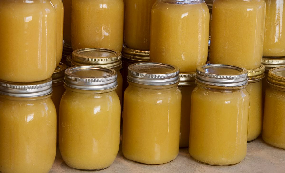 Rows of pint and quart jars filled with homemade canned applesauce, sealed with metal lids and stacked closely together on a counter.