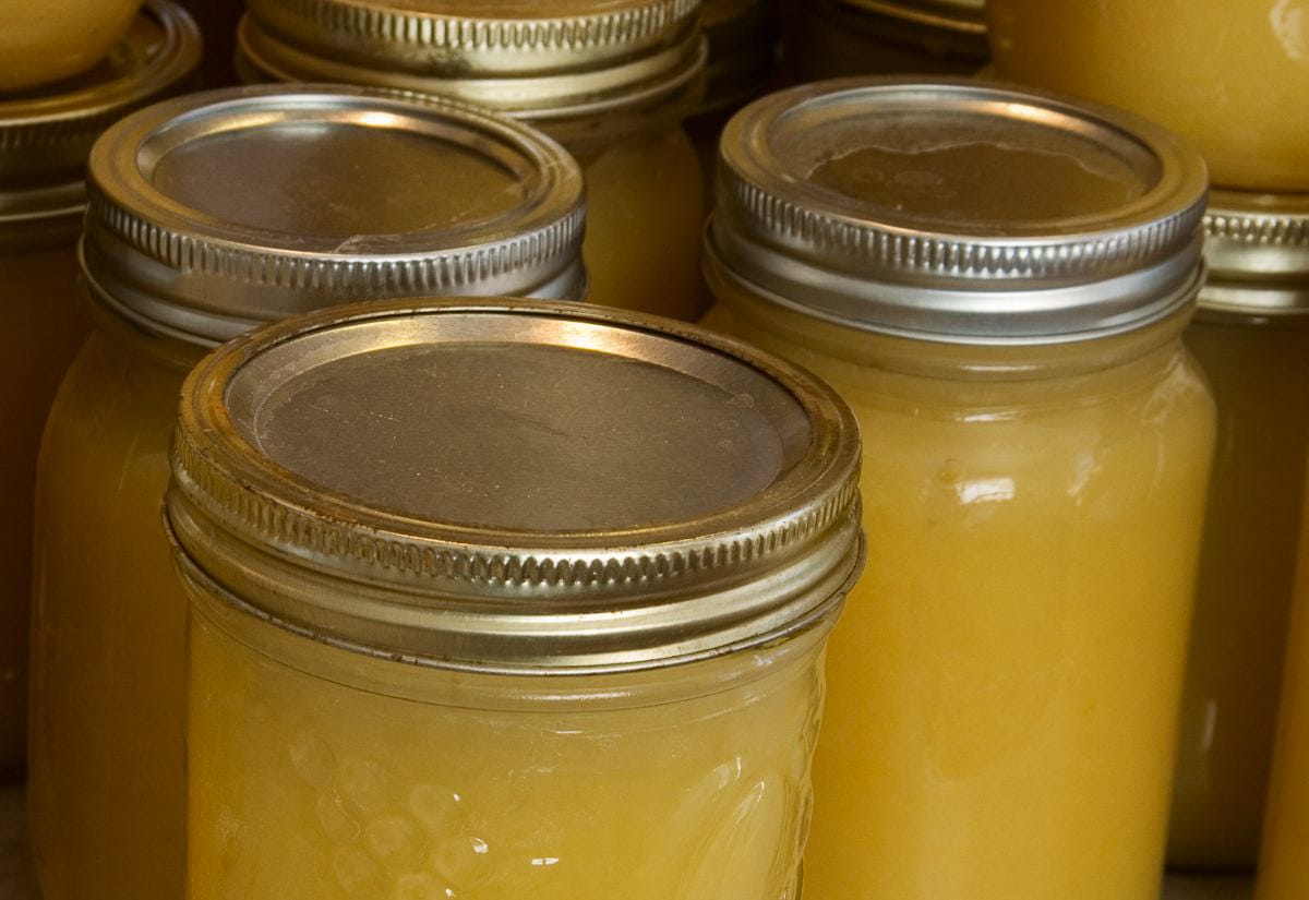 Close-up view of sealed mason jars filled with golden applesauce, showing the lids, jar rims, and smooth texture of the finished sauce.