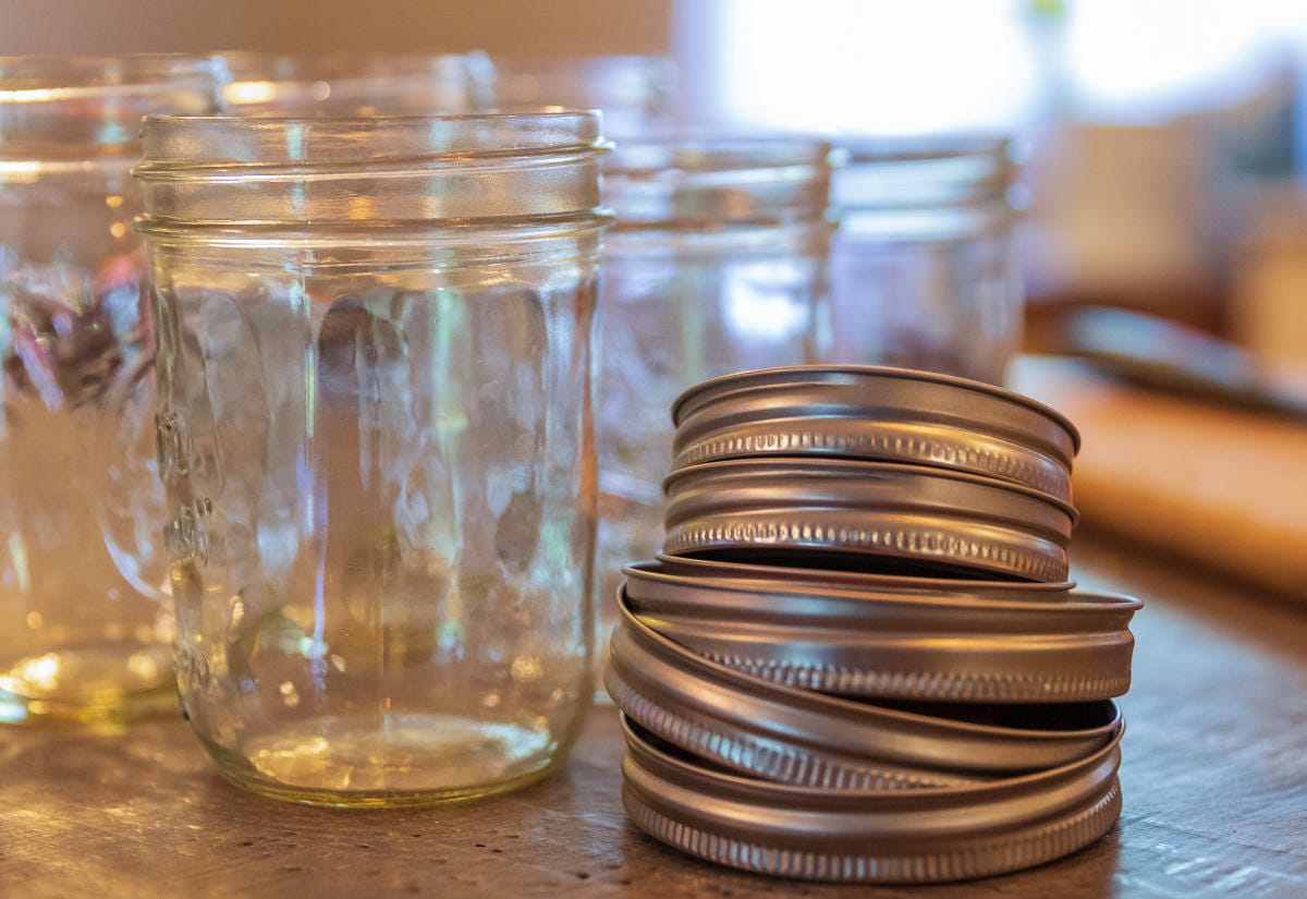 Stack of clean metal canning lids beside a row of empty mason jars on a kitchen counter, ready to be filled for water bath canning.