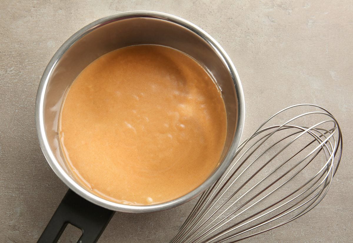A small saucepan filled with thick, homemade turkey gravy, sitting beside a wire whisk on a neutral countertop