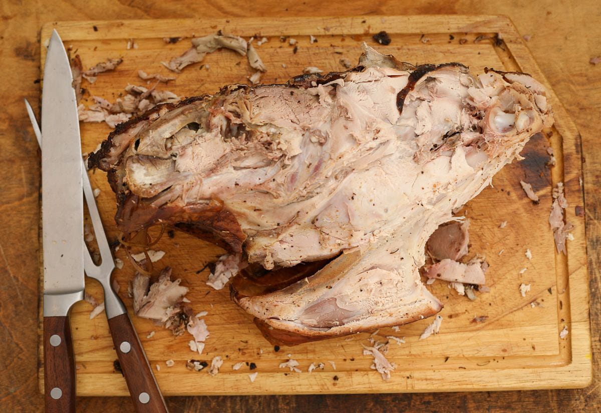 A roasted turkey carcass on a wooden cutting board beside a carving fork and knife — the starting point for making homemade turkey broth before simmering and canning.