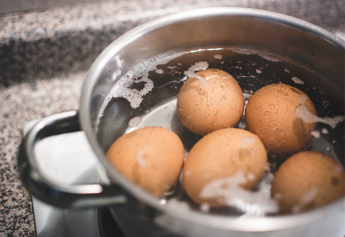 Brown eggs warming gently in a pot of water on the stovetop, shown mid-pasteurization with small bubbles forming around the shells.