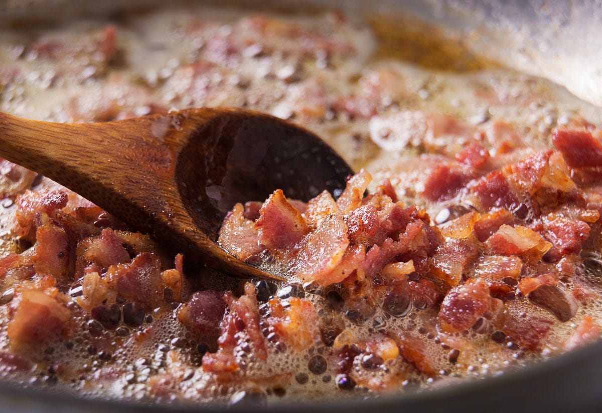 Chopped bacon cooking in a large pot, rendering fat for the base of homemade Maine-style corn chowder.