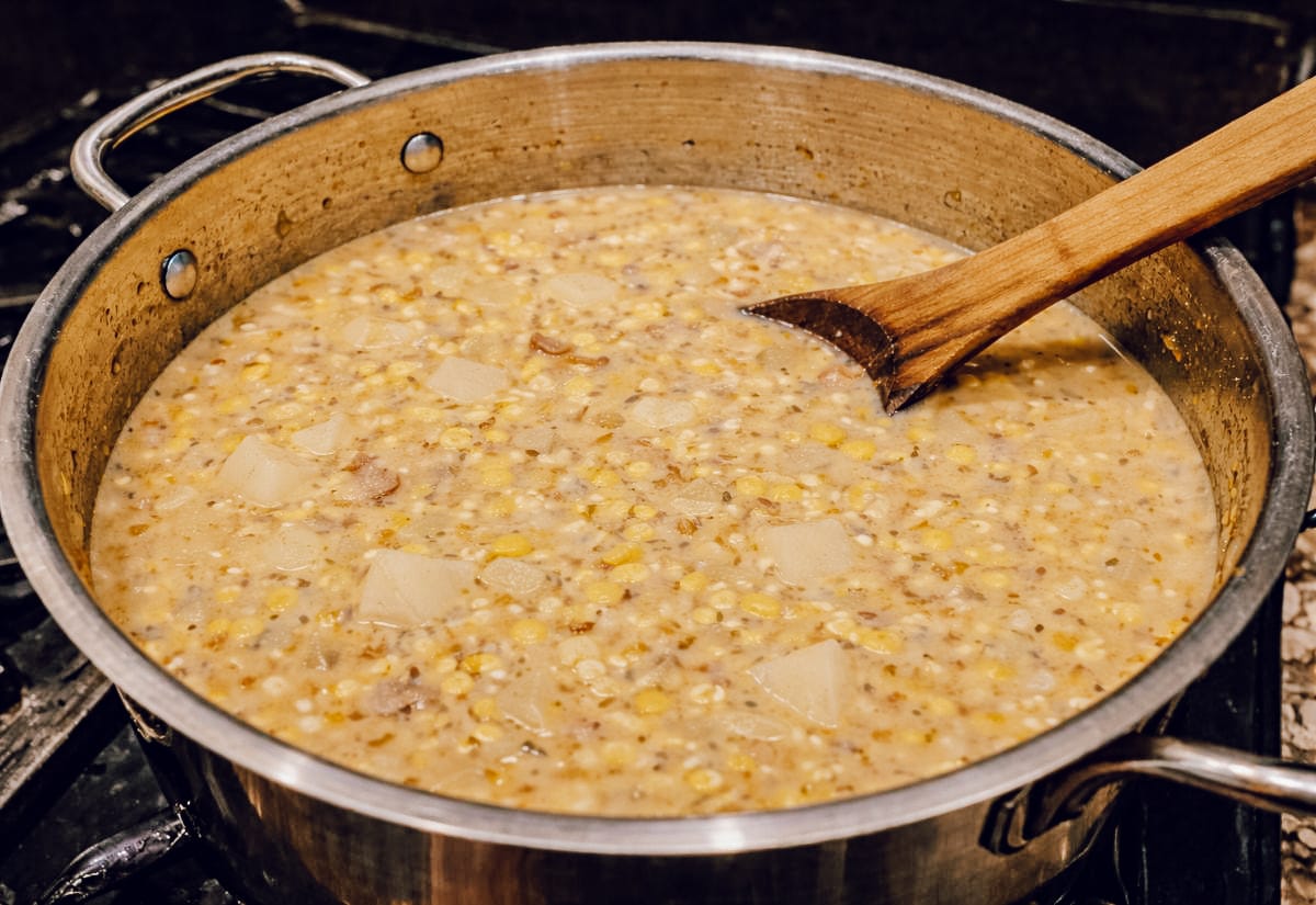 Corn chowder simmering in a large pot with potatoes, corn, and broth before the half-and-half is added.