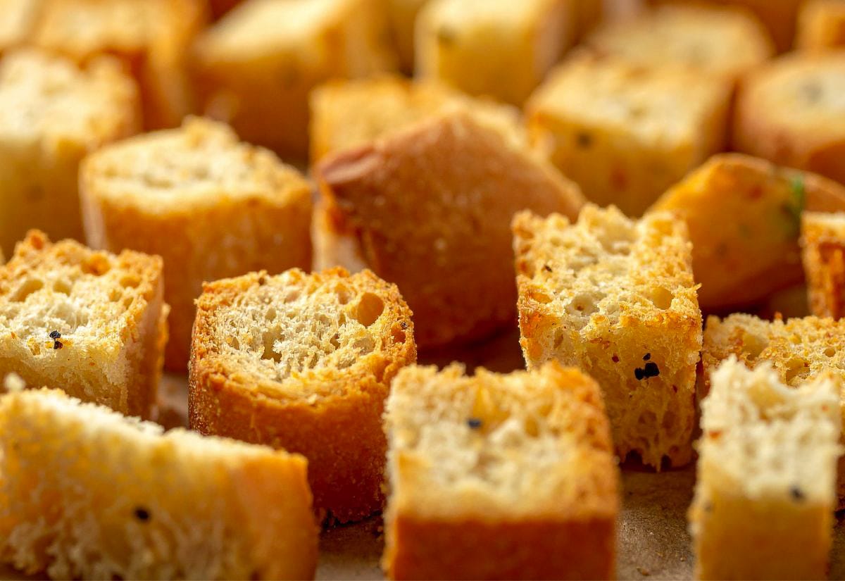 A close-up view of crunchy oven-baked croutons, highlighting the toasted exterior, airy interior, and specks of seasoning.