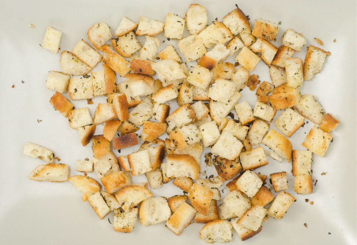 A spread of homemade croutons tossed with dried herbs on a light-colored surface, showing irregular sizes.