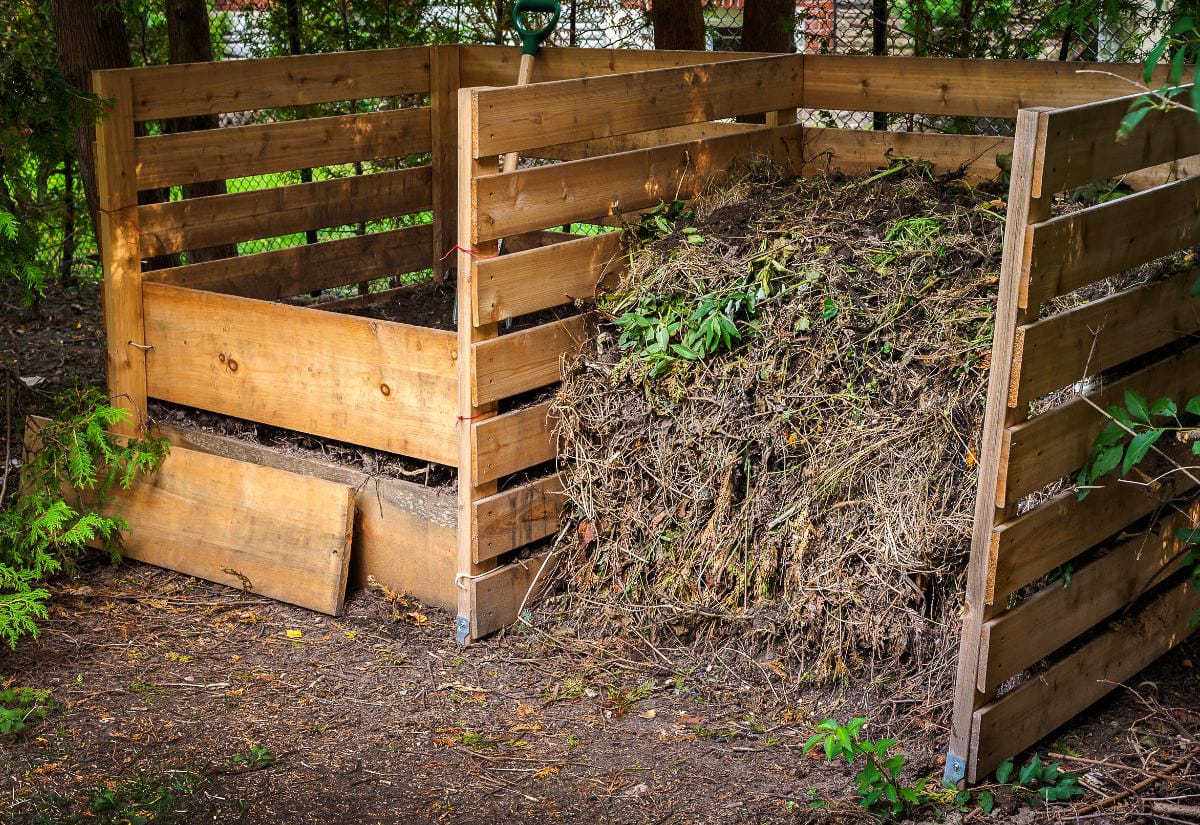 Two large wooden compost bins filled with decomposing garden waste, leaves, and plant material, showing an active backyard compost system.
