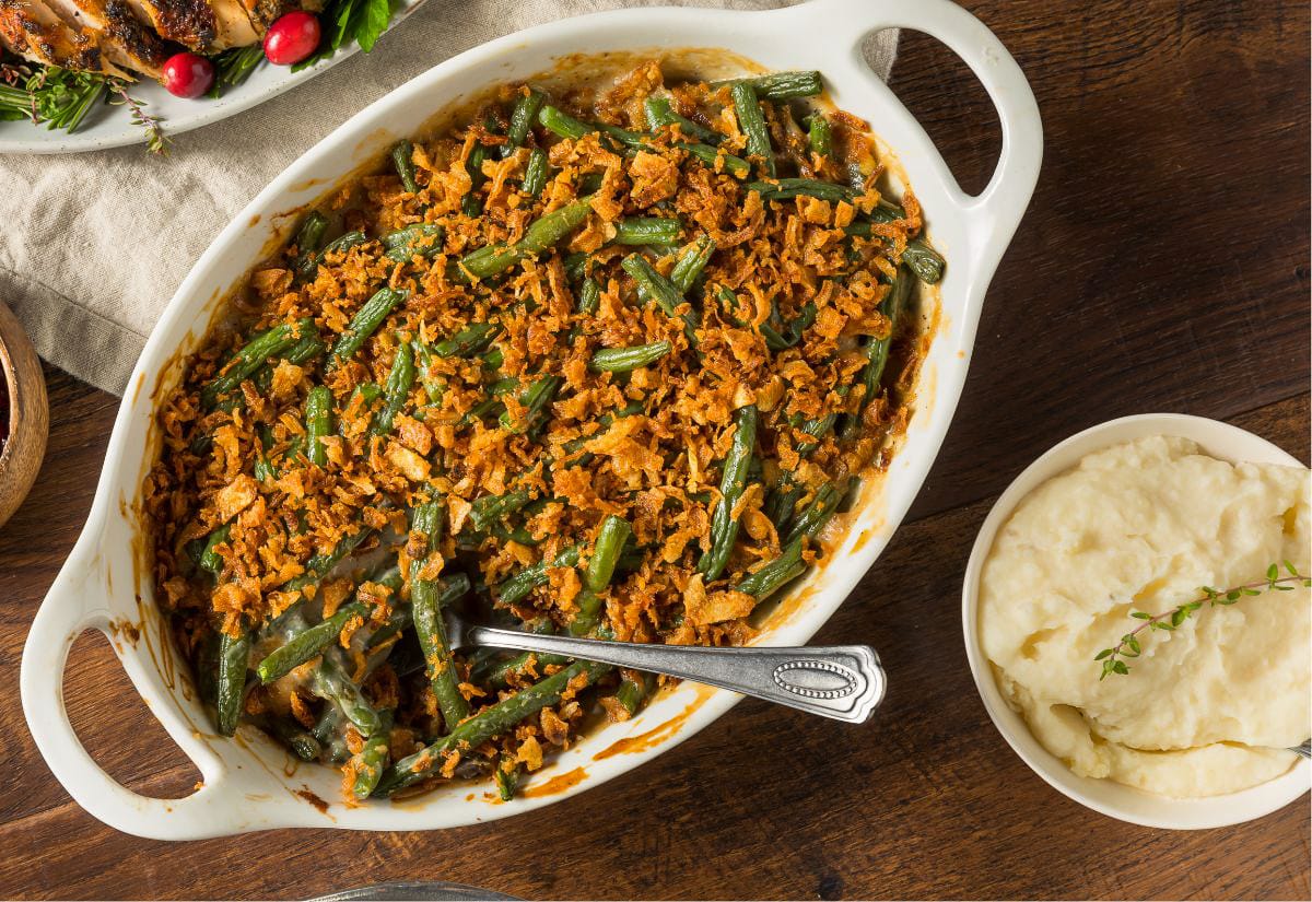 Green bean casserole topped with crispy onions served alongside a bowl of creamy mashed potatoes on a wooden table.